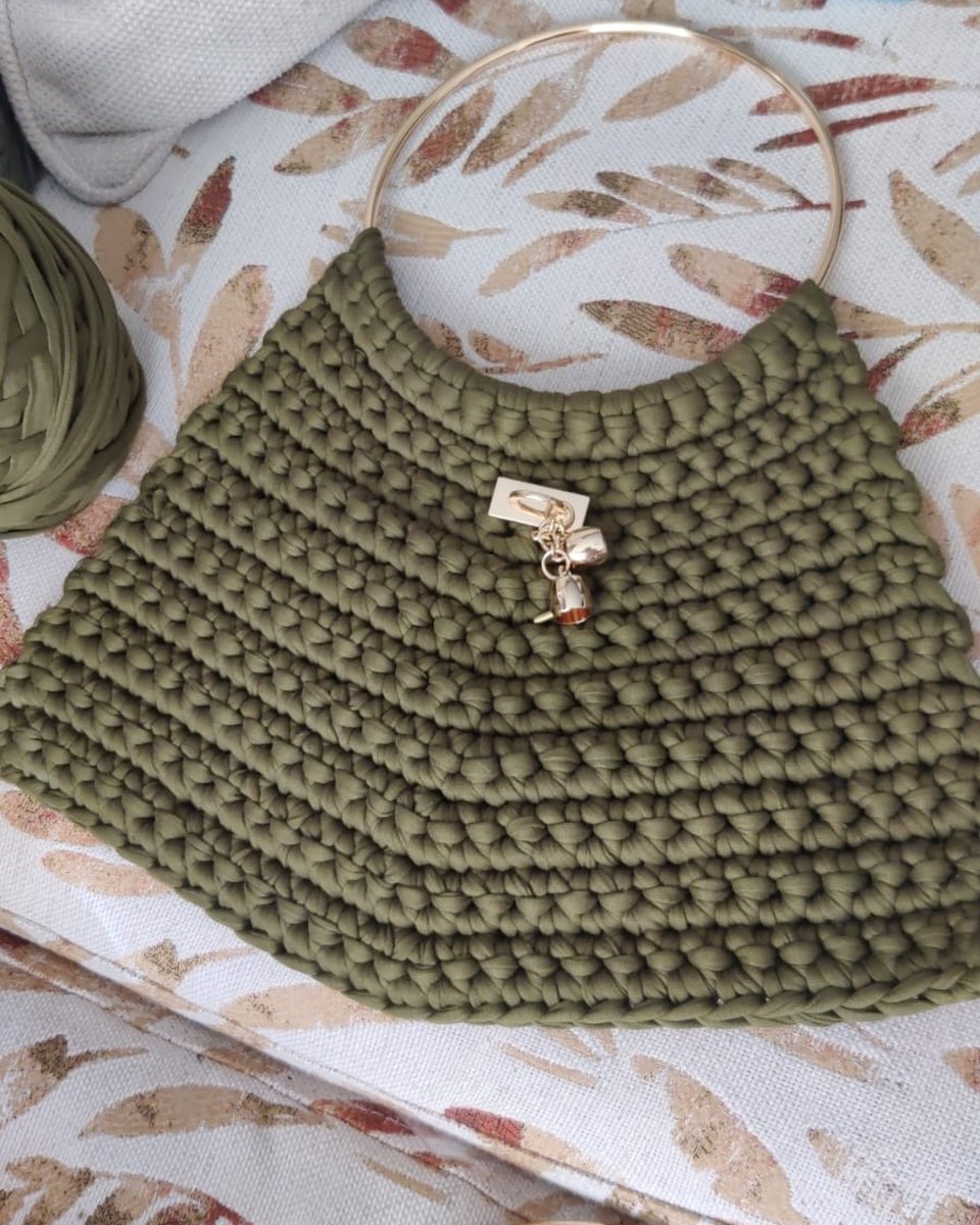 Bolso tejido verde olivo sobre la mesa, con un aro dorado y un ovillo de hilo al lado